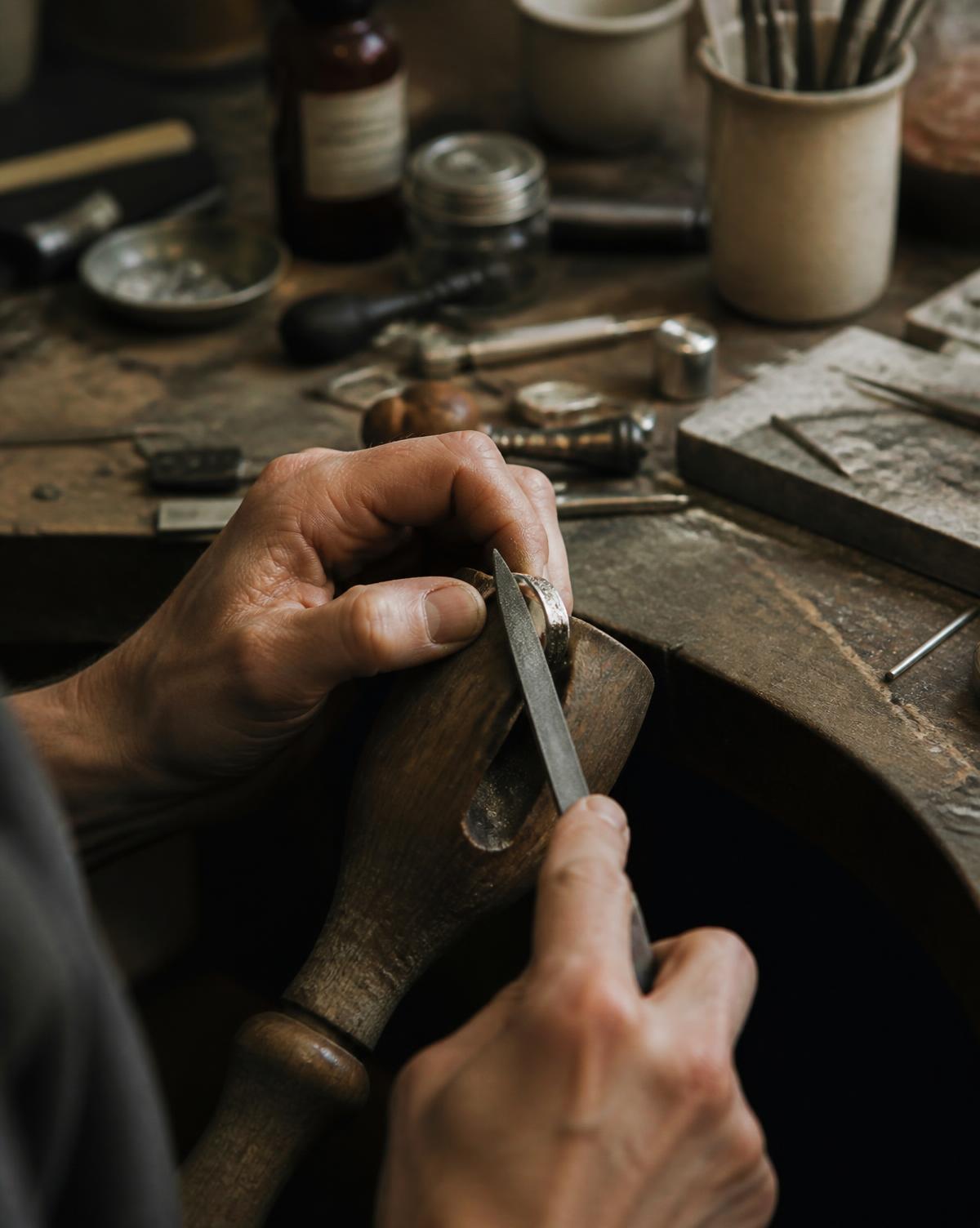 Kerry's hands filing a silver ring held in a wooden ring clamp at the workbench