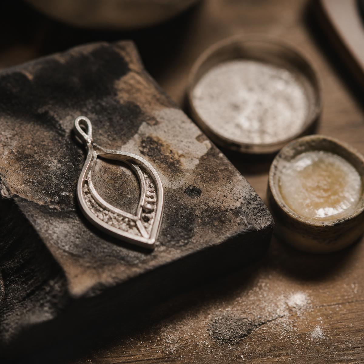 A part-finished silver pendant resting on a soldering block beside flux and solder